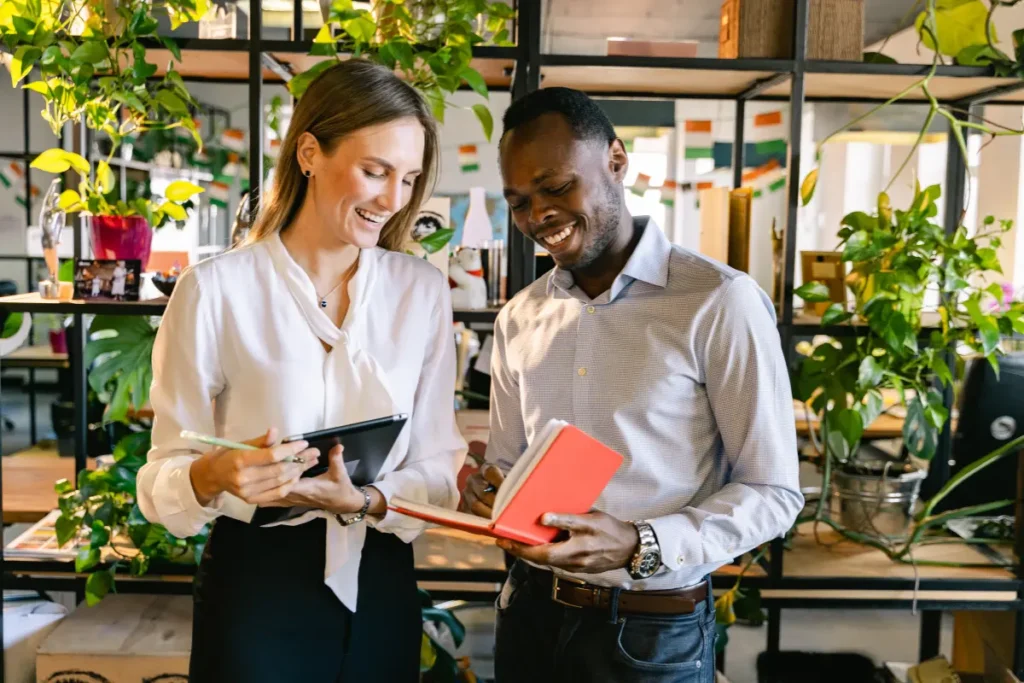 Two colleagues smiling while reading a book. 
