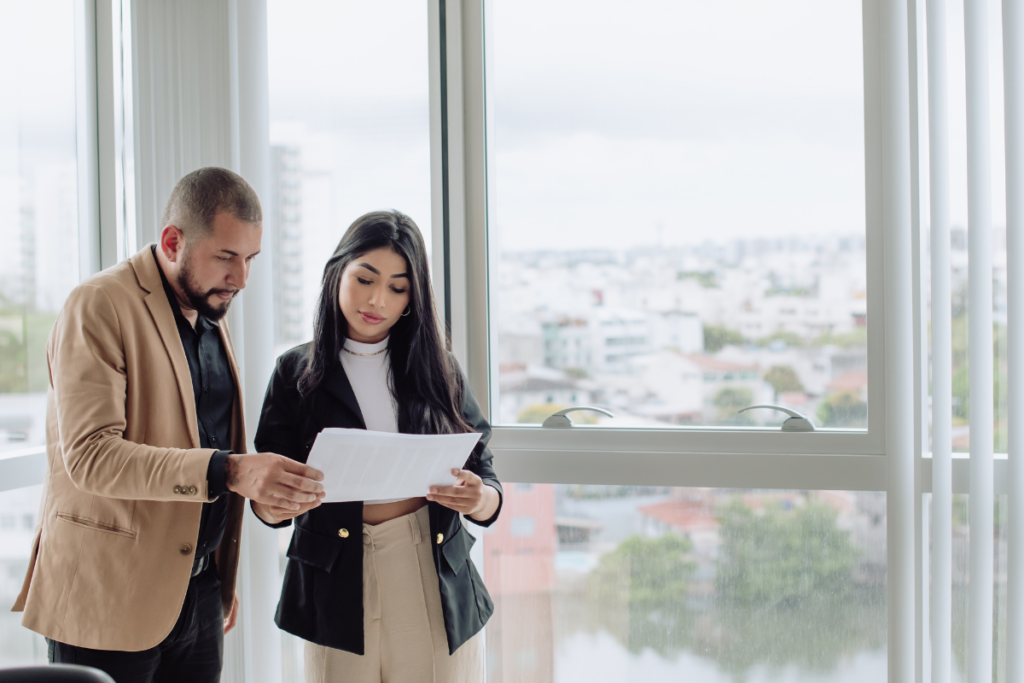 Coworkers review a document by office window.