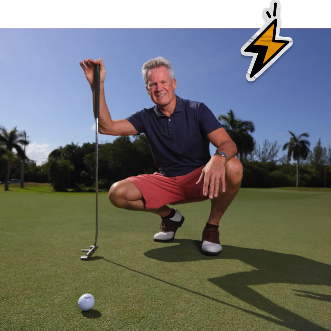 Man on golf green lining up a putt on a sunny day.