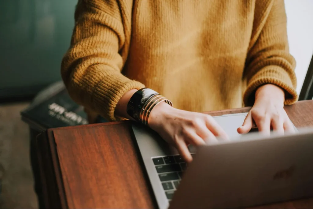 Person typing on a laptop while working at a wooden desk.