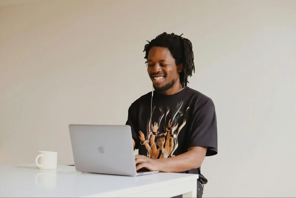 Smiling person standing and working on a laptop in a minimal workspace.