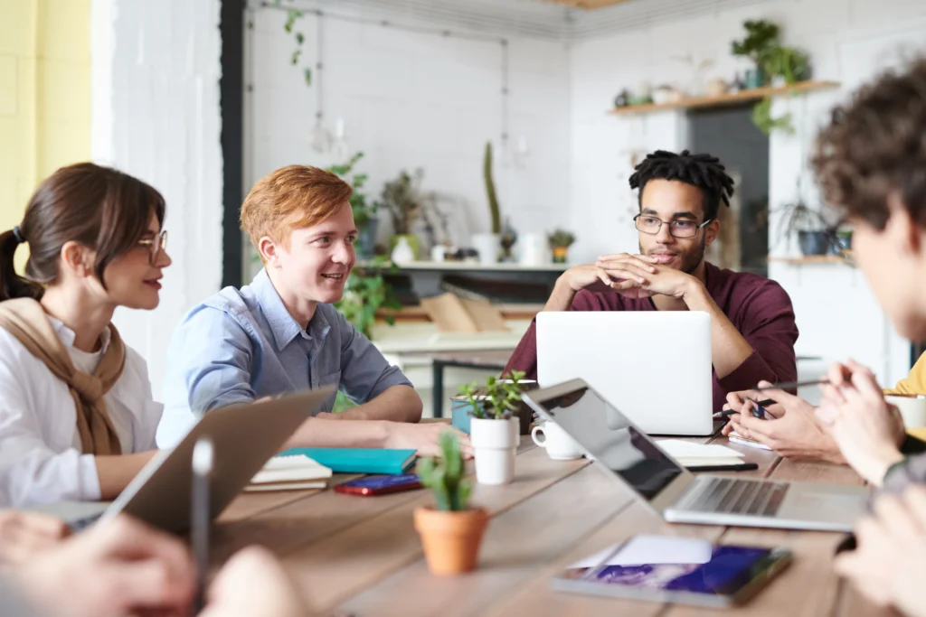 A group of employees sitting around a table in a modern office, collaborating and smiling during a meeting.