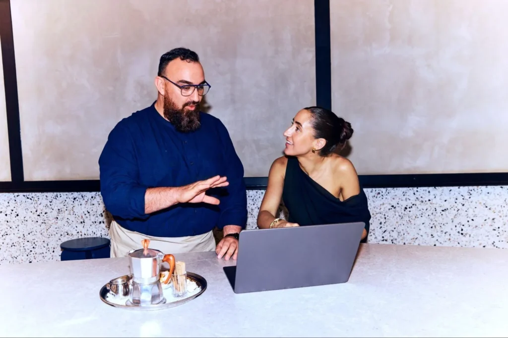 Two colleagues discussing work over a laptop at a modern workspace.
