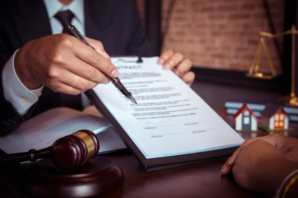Lawyer points to contract document while advising client at desk.