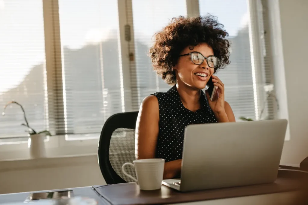 A woman on her phone while facing her laptop in the office