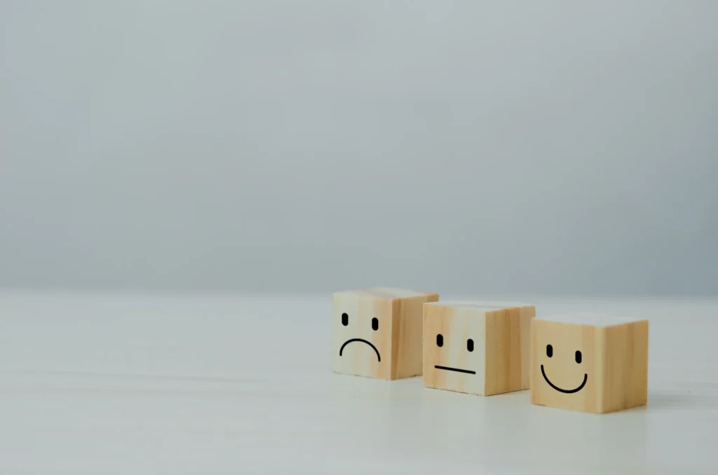 Wooden cubes displaying different facial expressions ranging from sad to happy, symbolizing customer satisfaction or employee feedback.