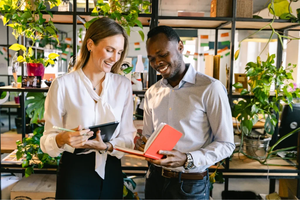 Two small business owners reviewing documents together inside a bright, plant-filled café or shop.