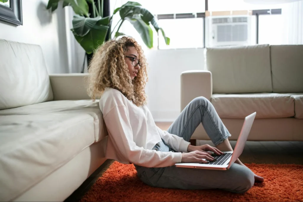 Woman sitting comfortably on the floor at home using a laptop with a coffee mug nearby.