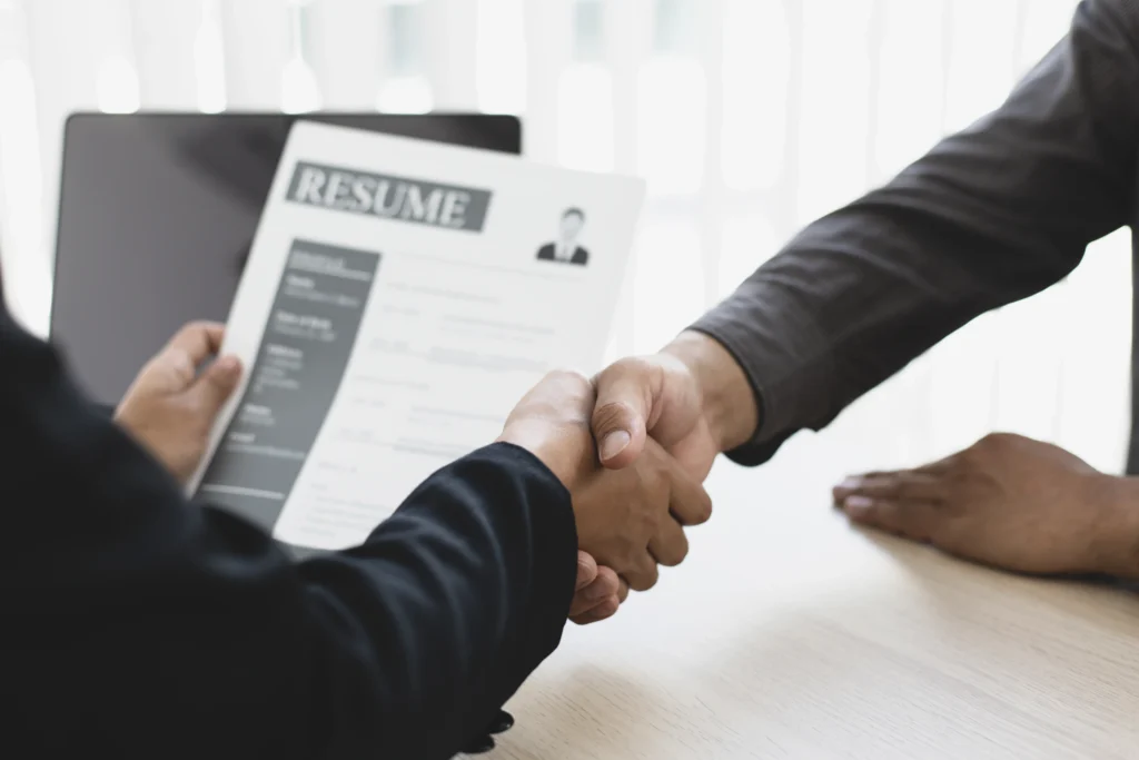 A recruiter reviewing a candidate’s resume while shaking hands during an interview, representing the best hiring platform process.