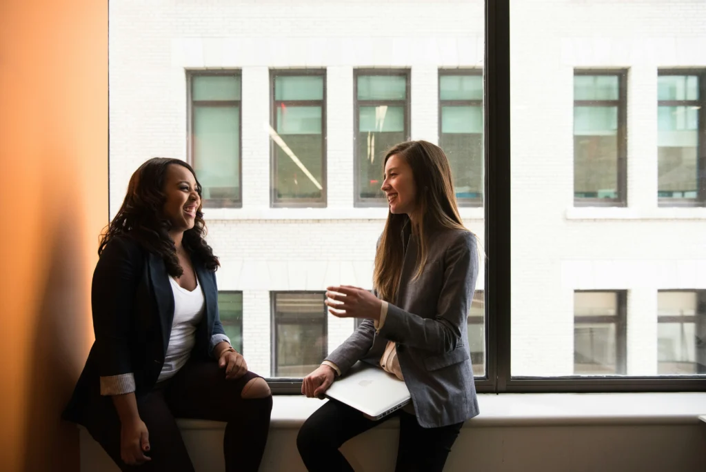 Two women engaged in conversation, sitting by a window with natural light illuminating their discussion.