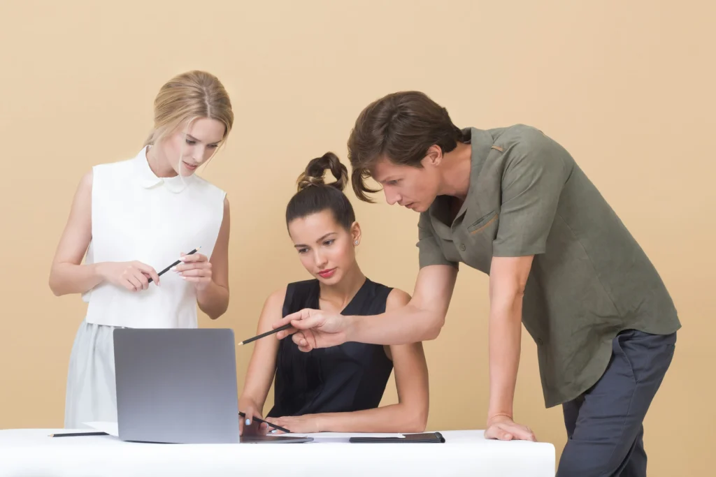 Three colleagues collaborating on a laptop in a modern office setting.
