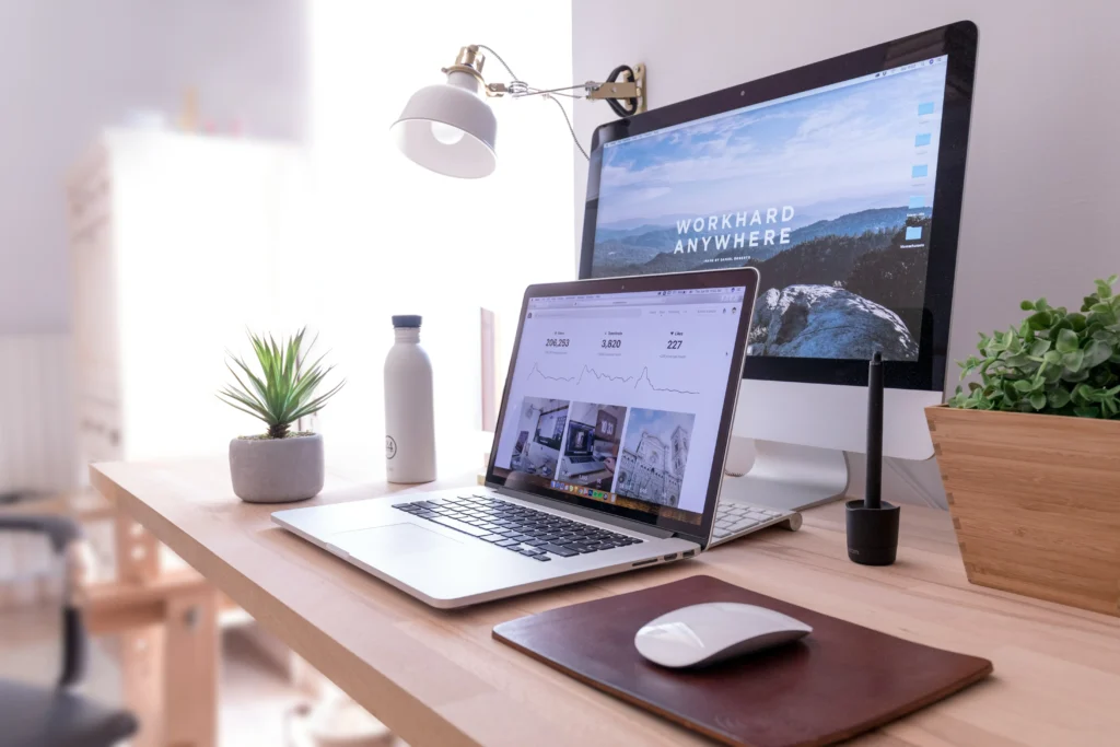 A clean remote work desk setup with a laptop, desktop monitor, and plants, symbolizing remote worker productivity.