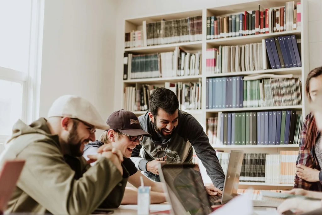 Group of young adults studying together and laughing while working on laptops in a library