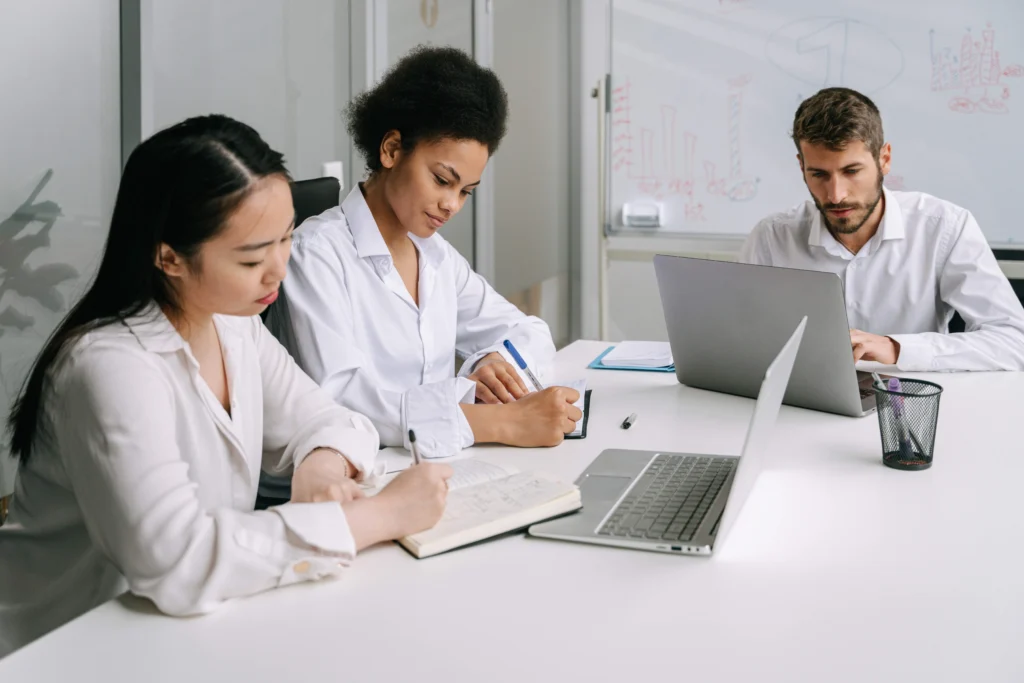 Three people seated at a table, collaborating over a laptop in a casual setting.