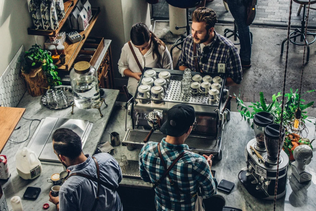 A group of people gathered around a coffee machine, engaging in conversation and enjoying their drinks.