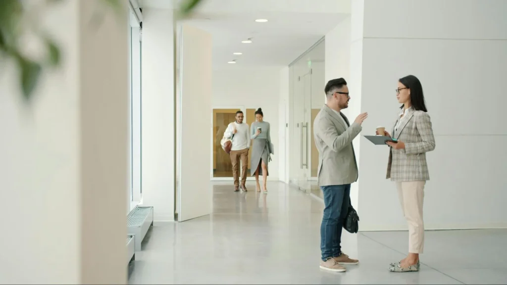 Two people engaged in conversation standing in an office hallway