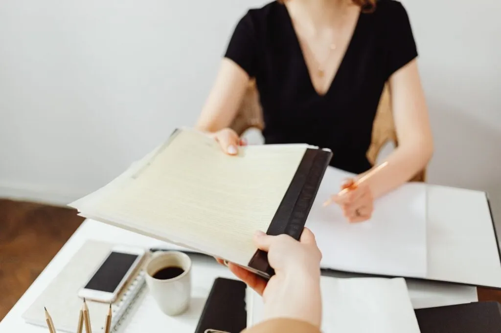 Document handoff at desk with coffee, phone, and writing tools in professional setting