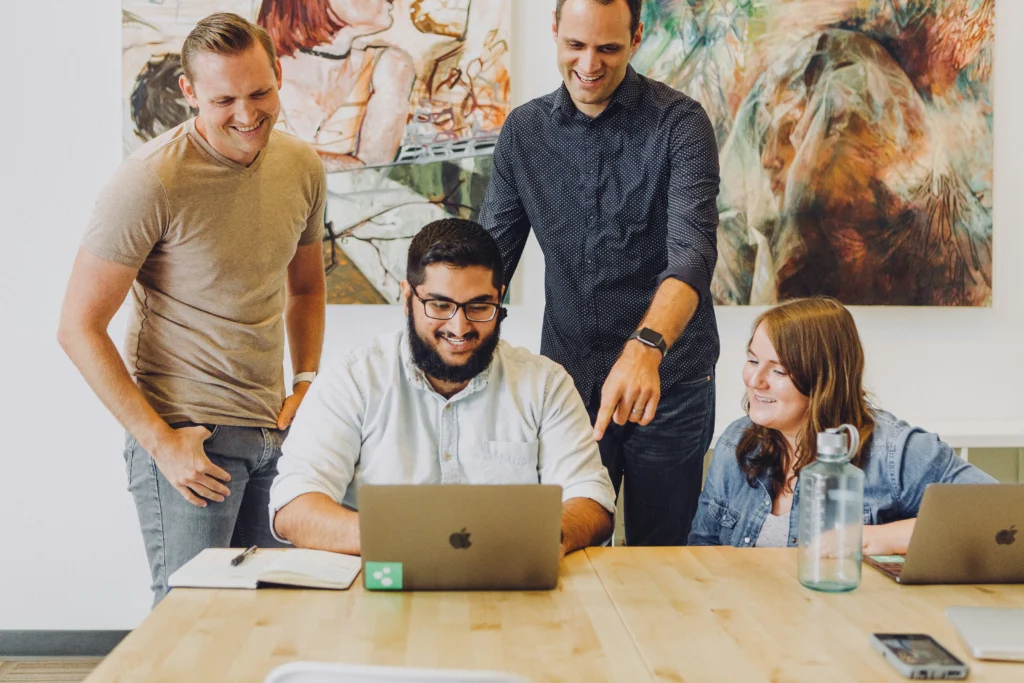 Colleagues surrounding a man working on his laptop