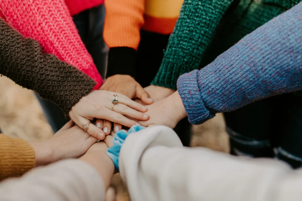 A close-up of diverse individuals putting their hands together in a huddle, illustrating the teamwork and collaboration that AI for non-profit organizations can help leaders foster.