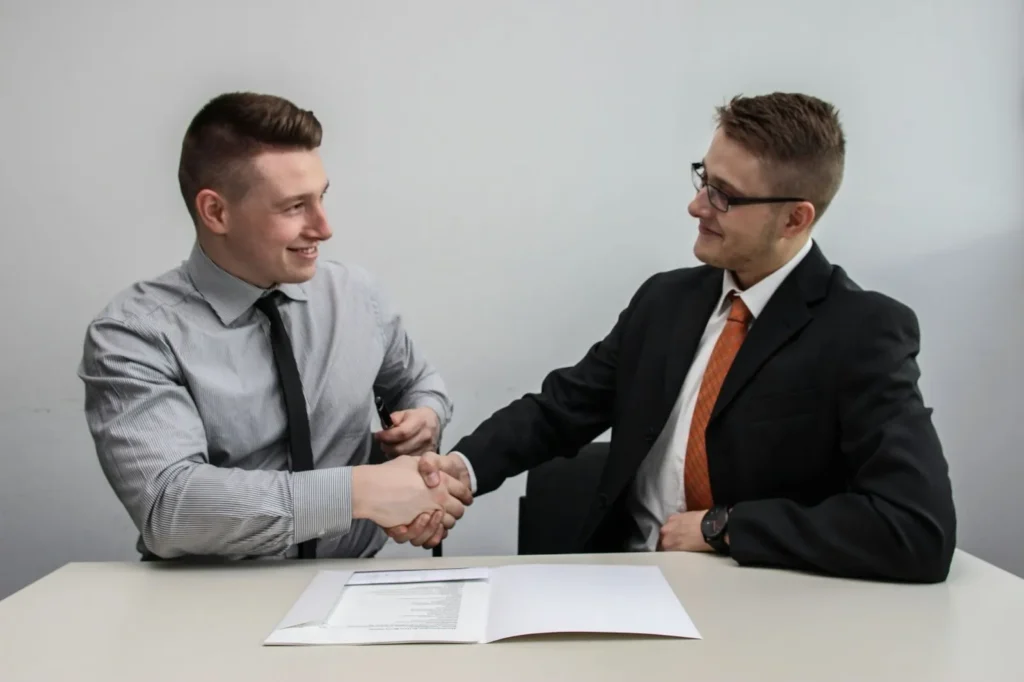 Two businessmen shaking hands over a signed document, representing a successful external recruitment process and job offer acceptance.