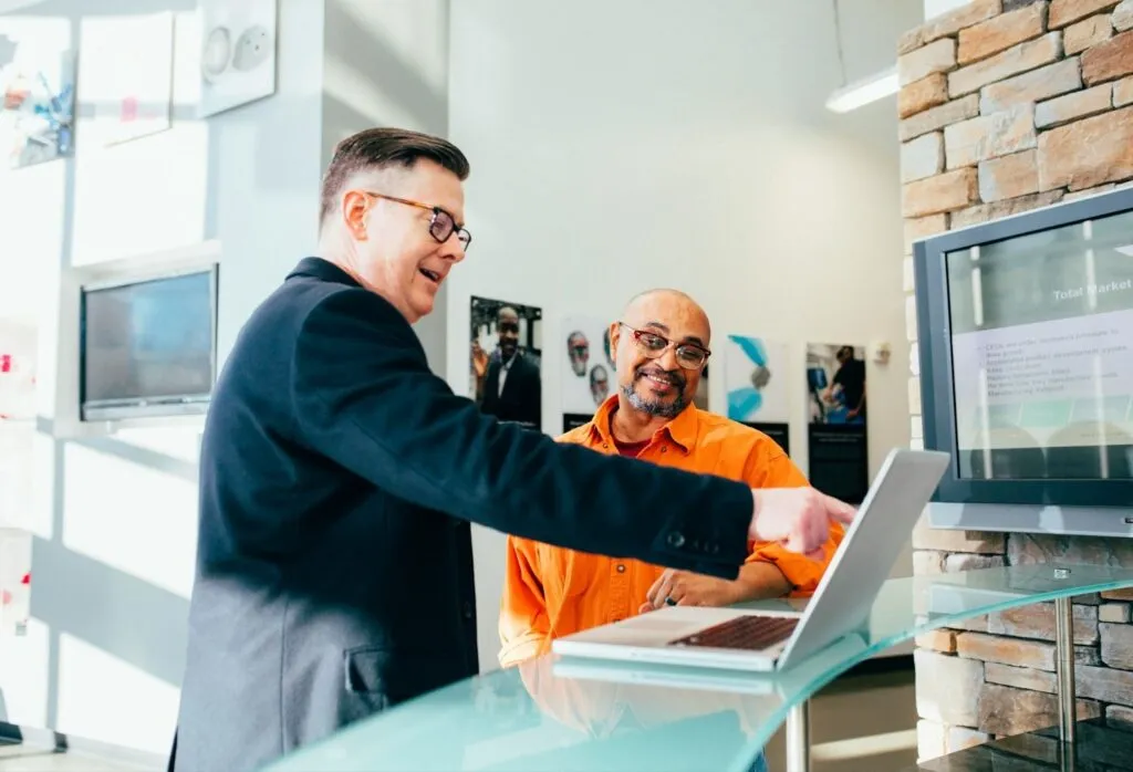 Two professionals discussing information on a laptop in an office, representing an employer and employee reviewing company policies for leave without pay in Canada.