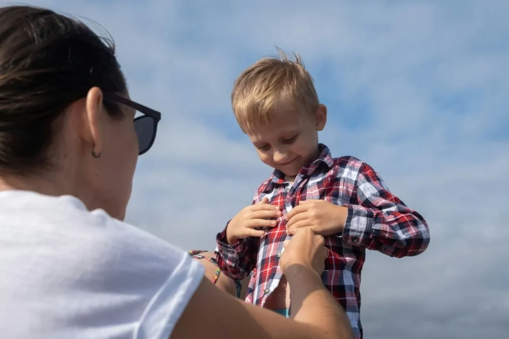 A mother adjusting her young son's shirt outdoors, illustrating family responsibilities and childcare as common reasons employees might request leave without pay in Canada.