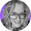 A smiling person with wavy hair and large glasses appears in a black-and-white close-up with a vibrant purple background, conveying a cheerful mood.
