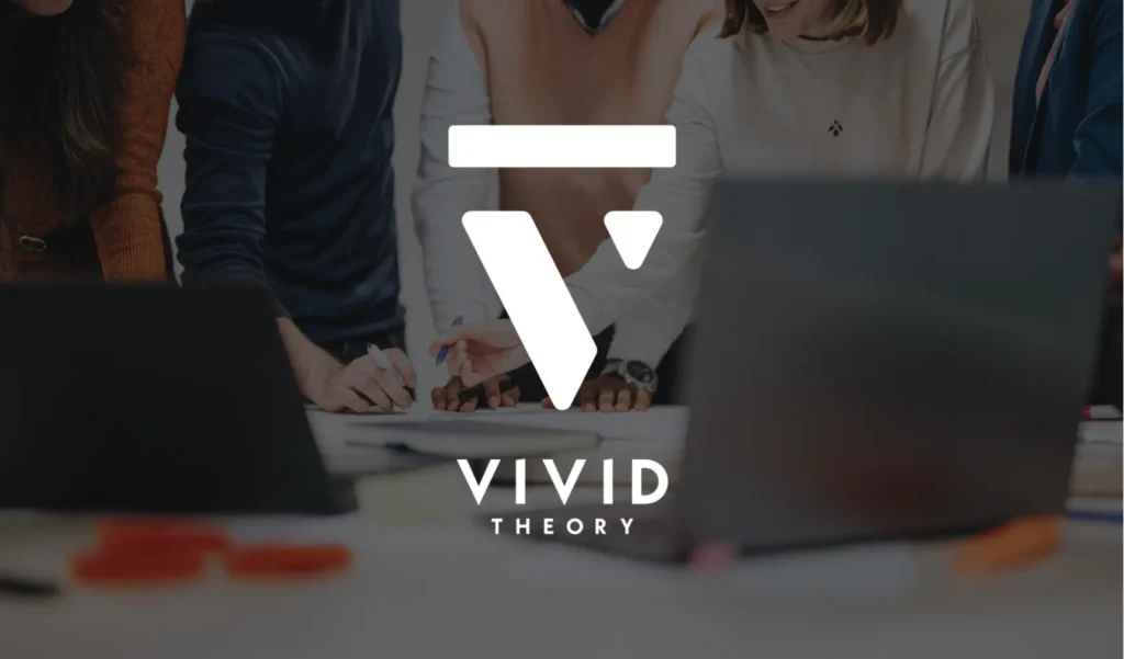 A diverse team collaborates around a table with laptops and documents. Overlayed is the white "Vivid Theory" logo, conveying innovation and teamwork.