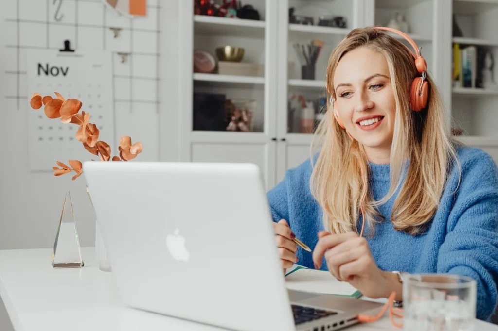Woman wearing headphones, smiling as she works on her laptop