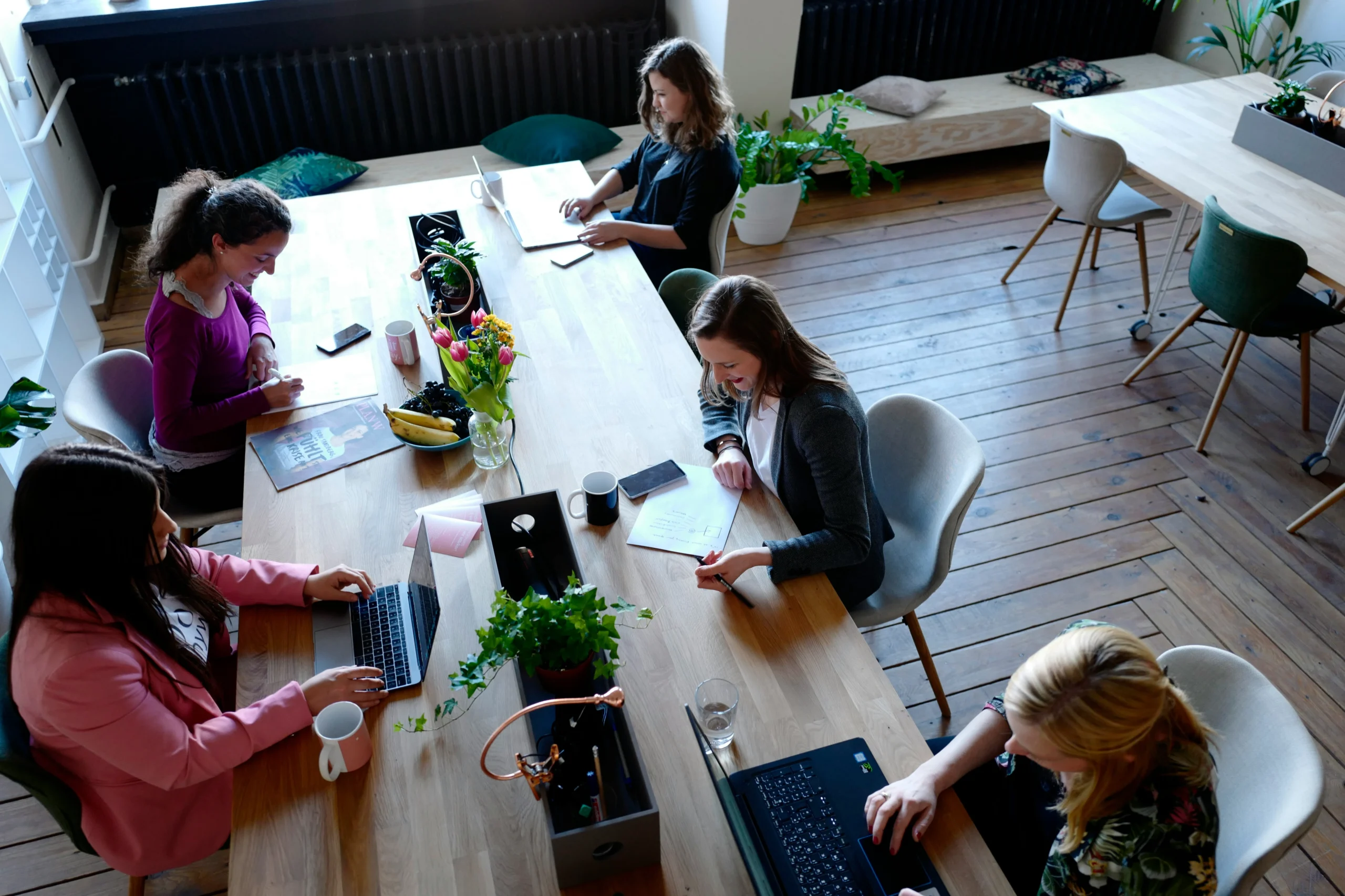 A group of diverse individuals seated at a table, each using a laptop for collaborative work or discussion.