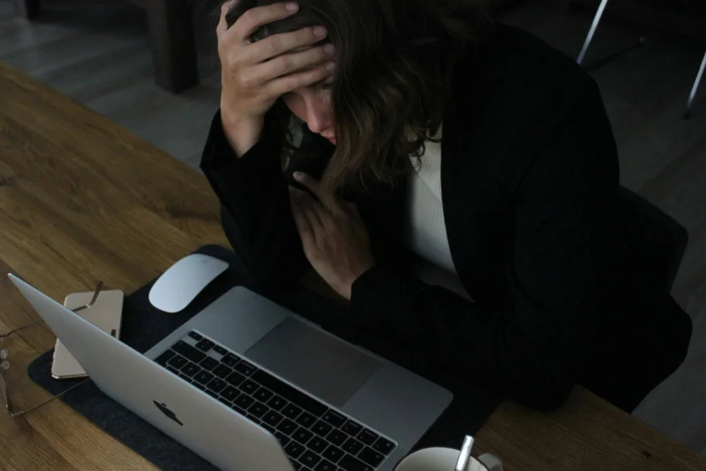 A woman with her hand on her forehead as she works on her laptop