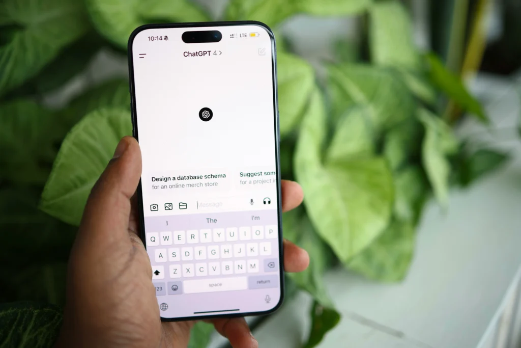 A hand holds a smartphone displaying a ChatGPT 4 app with a keyboard interface. The background shows vibrant green leaves, creating a fresh and tech-savvy ambiance.