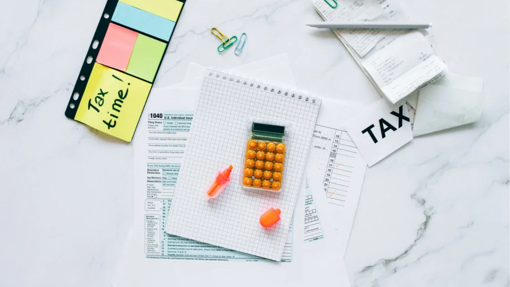 An overhead shot of tax forms, receipts, a calculator, and a sticky note reading "Tax time!" arranged on a marble surface.