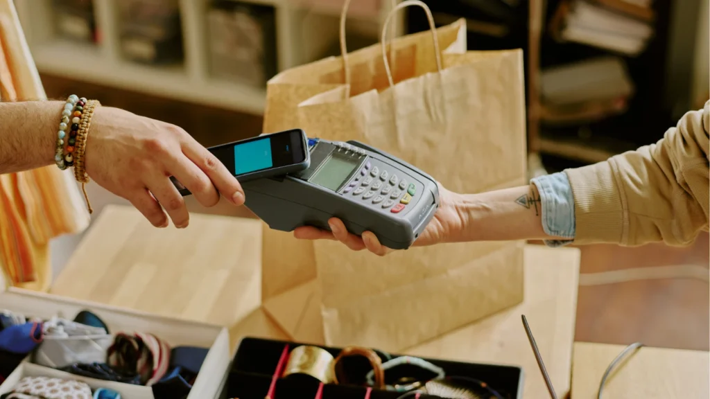 A customer uses a smartphone to make a quick contactless payment on a handheld card reader held by a store clerk at a retail register.