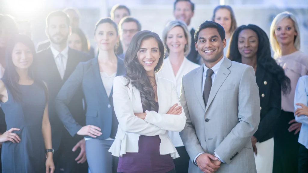 A diverse group of smiling business professionals standing together in a brightly lit office setting.