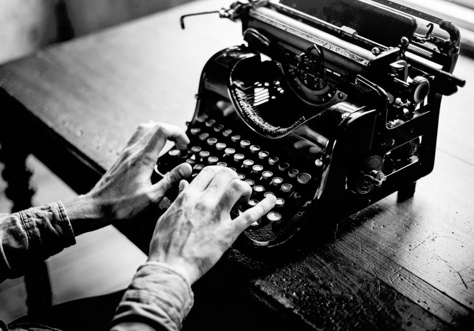 A black and white image of a person writing on a traditional typewriter.