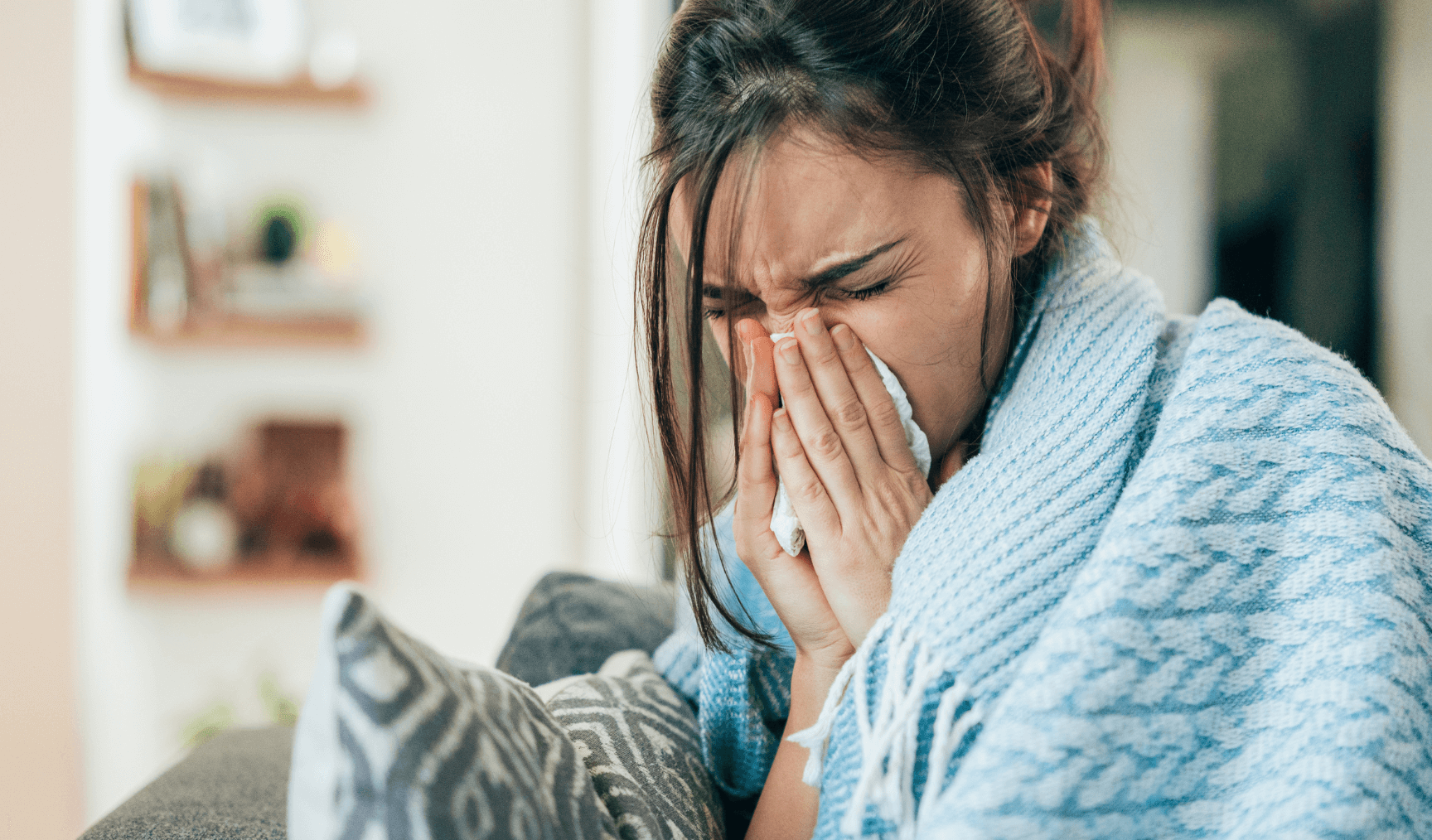 sick woman sneezing into some tissues