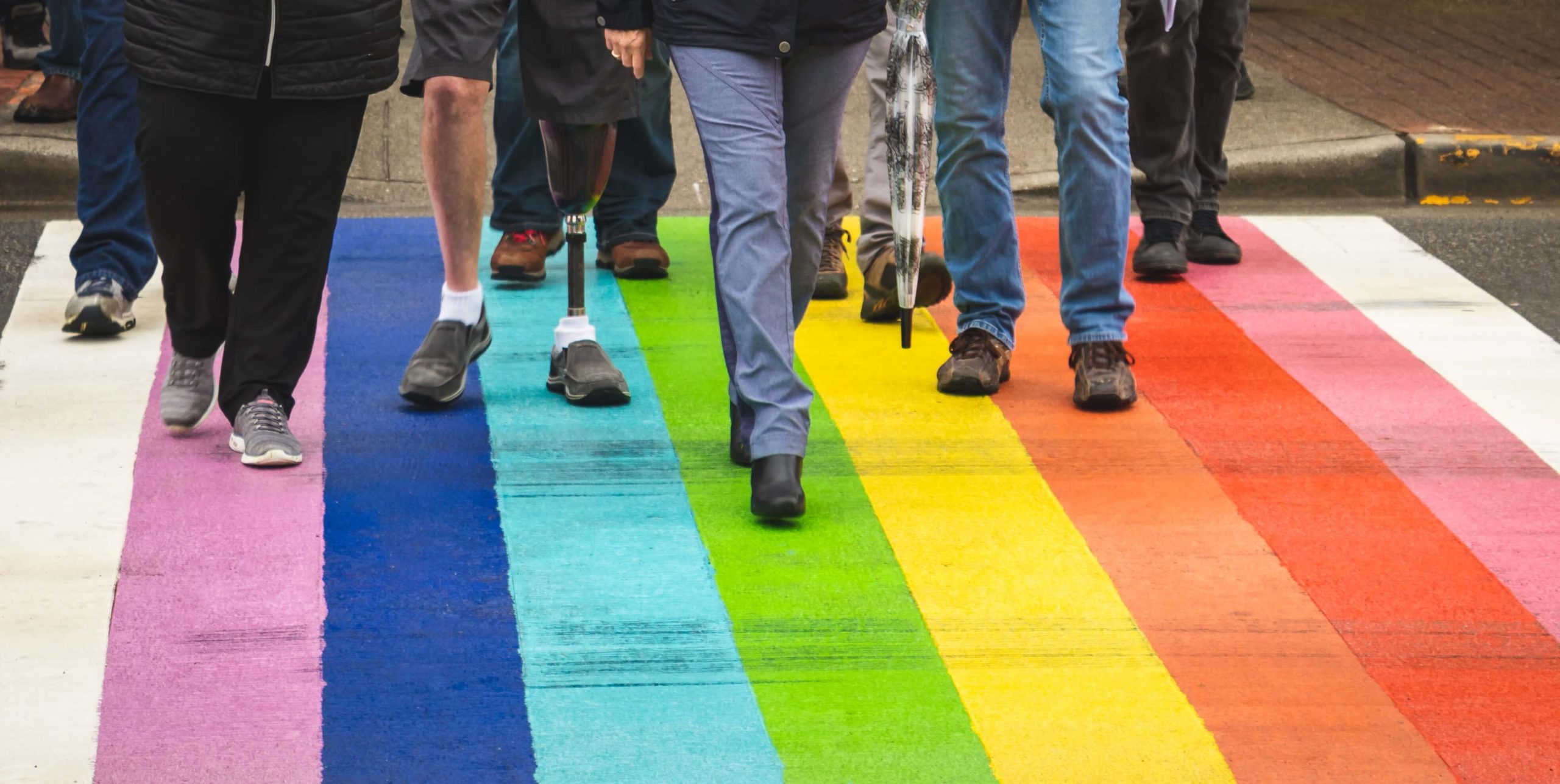 People representing diversity walking across a rainbow flag