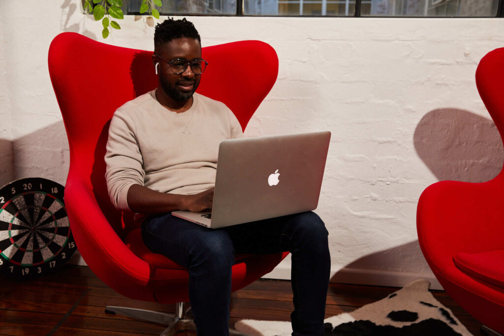 A man sitting on a red chair with a laptop on his lap