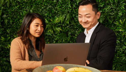 two colleagues sitting at a table looking at the same laptop against a vertical garden wall