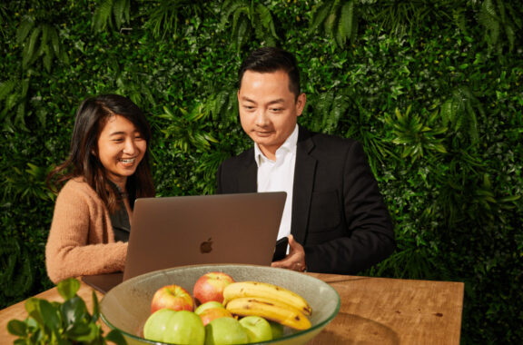 Colleagues reading off a laptop in front of a fruit bowl