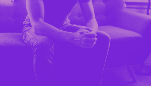 Man sitting on couch with hands clutched.