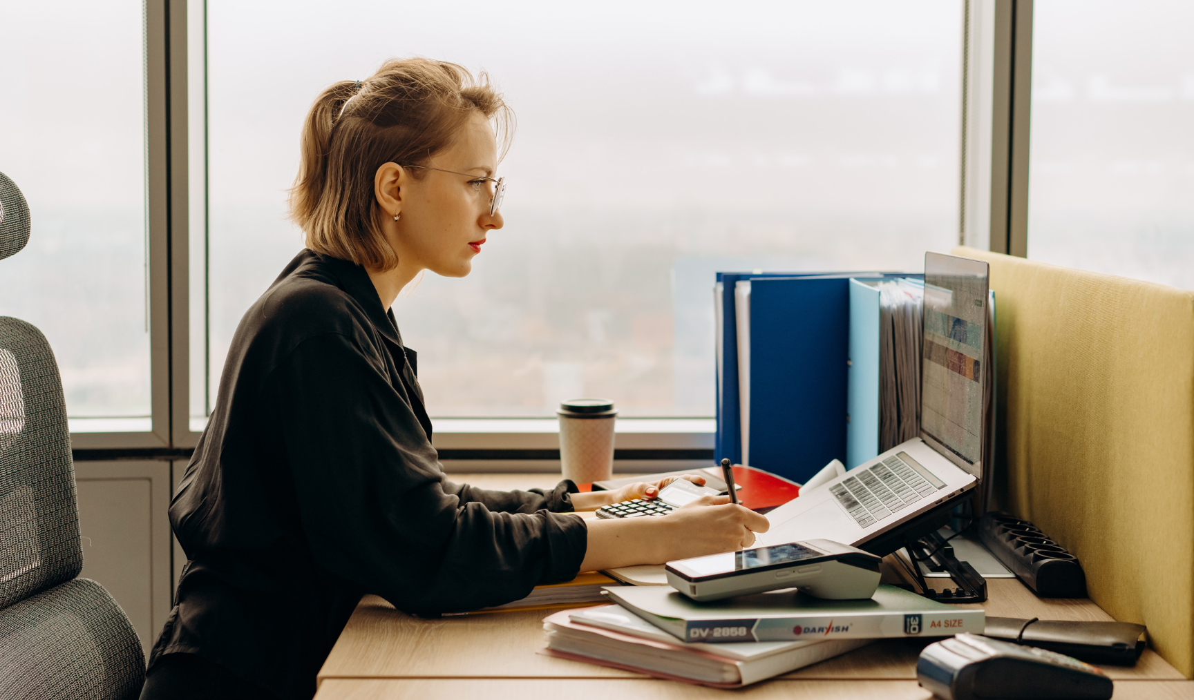 Woman working at desk, surrounded by paper and coffee