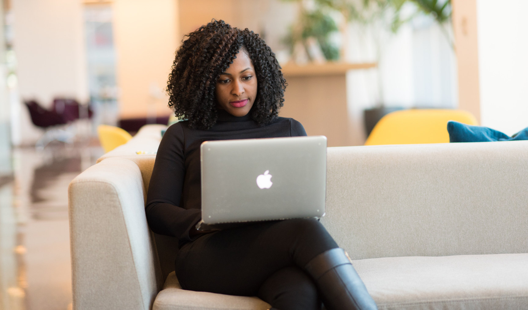 Woman sits on a beige sofa, with her laptop on her lap