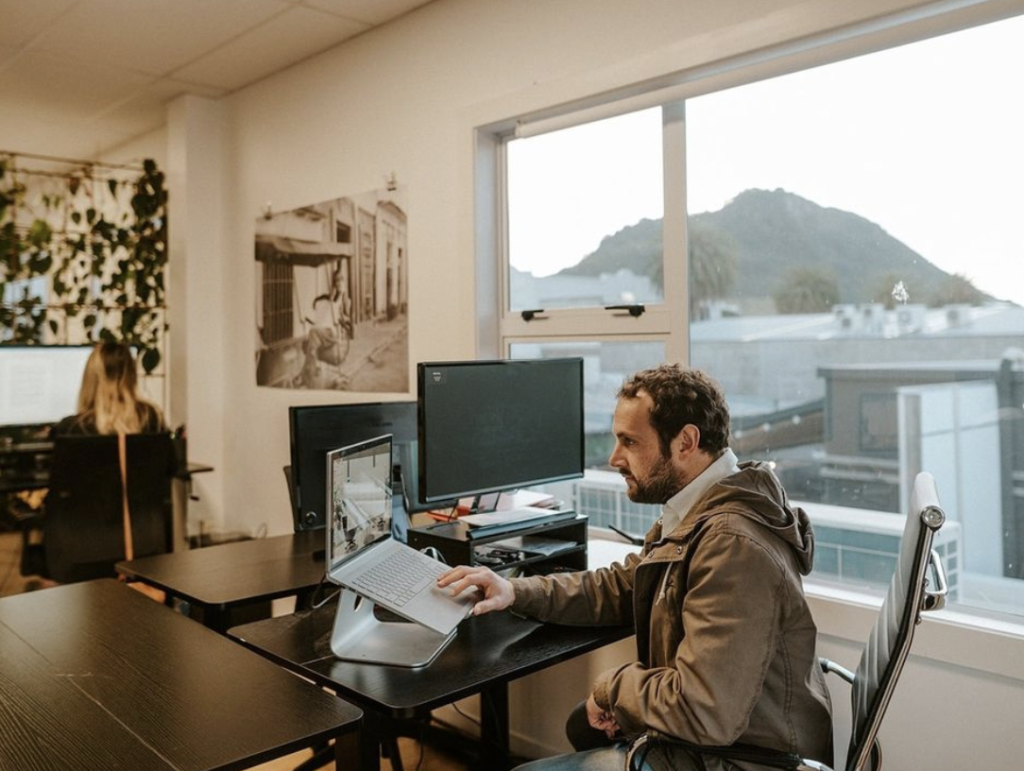 A person sitting at a desk in an office, with a view of a mountain through the window