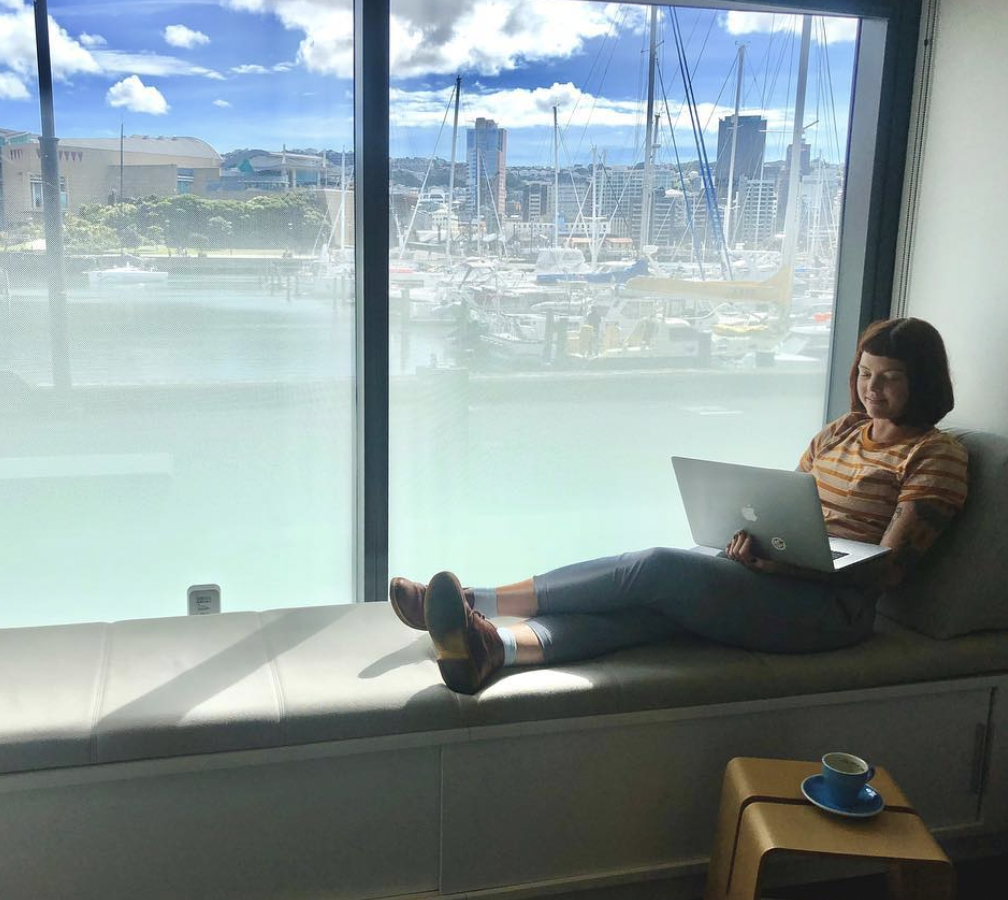 Person sitting casually on window bench, working on a laptop