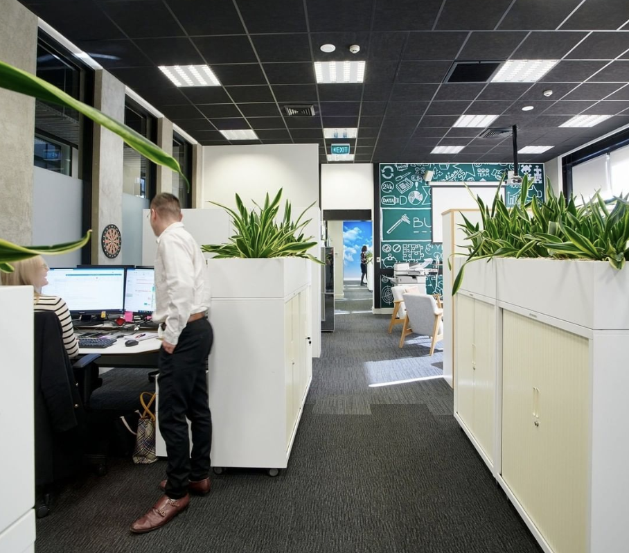 Large coworking space, one person works at a computer while another person stands next to them chatting