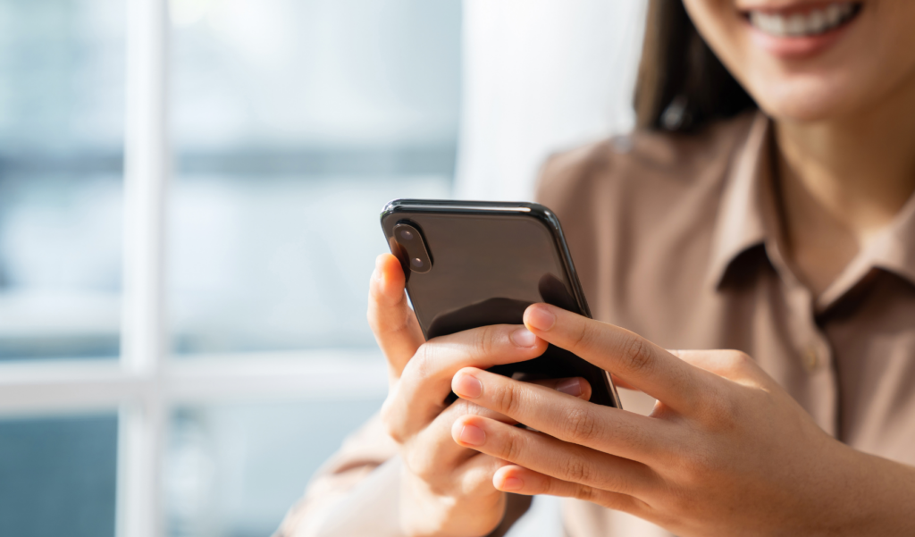 An image of a woman smiling as she holds her phone