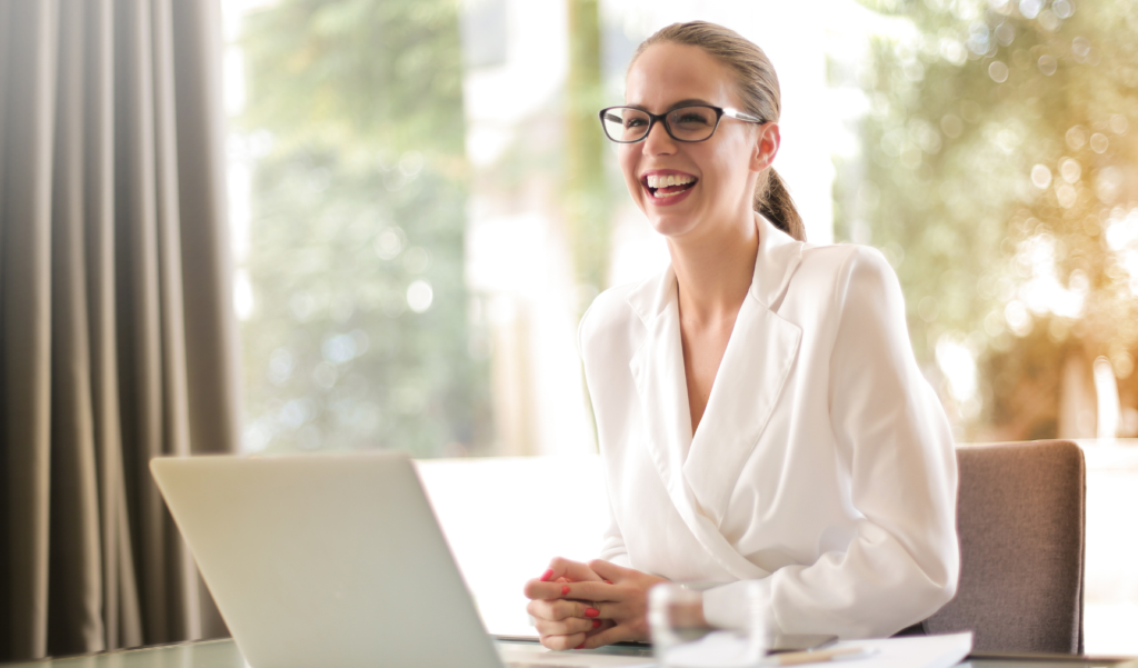 Woman sits at laptop smiling in a bright room