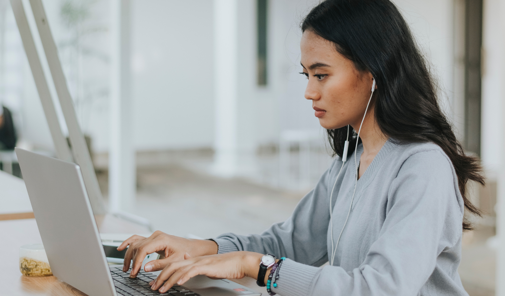 Woman sits at a laptop, earpods in, focused
